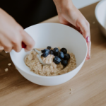 is oatmeal healthy , Close-up of a woman mixing oats flour, banana and blueberries in a bowl. Female making healthy breakfast in kitchen.